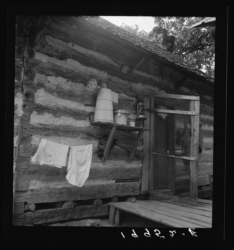 Porch on Negro share tenant cabin. A double one. Note the churn, lantern, baby's milk, and roof type. The other half of the cabin has a new galvanized metal roof. Near Gordonton, North Carolina