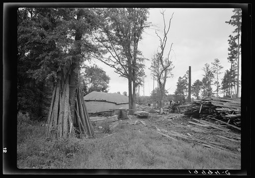 Small portable sawmill, very typical of the sawmills which are cutting small pine and hardwood growth of the area. Note mill and boiler, sawdust pile, stacks of slabs (or outsiders) located in fringe of trees between the highway and a corn field. Near Chapel Hill, North Carolina