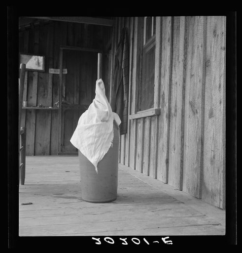 Untitled photo, possibly related to: Pottery butter churn on porch of Negro tenant family. The churn is covered with a cloth to keep the flies out. Note chair seat of split white oak. Chair making is a local craft long developed in this region. Randolph County, North Carolina
