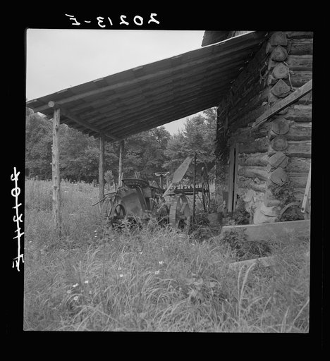 Farm machinery drawn under cover of old tobacco barn. Person County, North Carolina