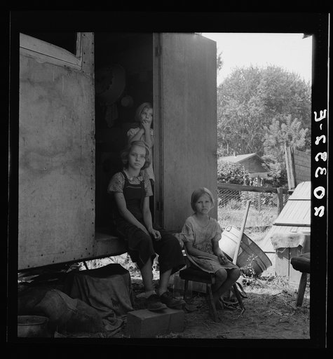 The oldest girl seated in the doorway of the house trailer cares for the family. Yakima Valley, Washington