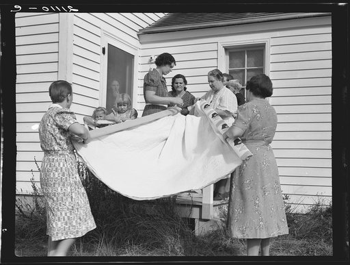 Farm women, members of the "Helping Hand" club, carefully roll up the quilt upon which they are working. Near West Carlton, Yamhill County, Oregon. General caption number 58-11
