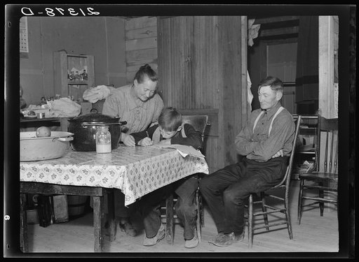 The Wardlow family in their dugout basement home on Sunday. The youngest boy copies out a recipe for his mother. Dead Ox Flat, Malheur County, Oregon