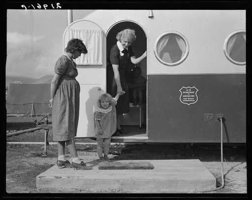 Young mother brings her child to the trailer clinic on the day when the doctor will be in camp to examine some of the children. FSA (Farm Security Administration) mobile camp. Merrill, Klamath County, Oregon