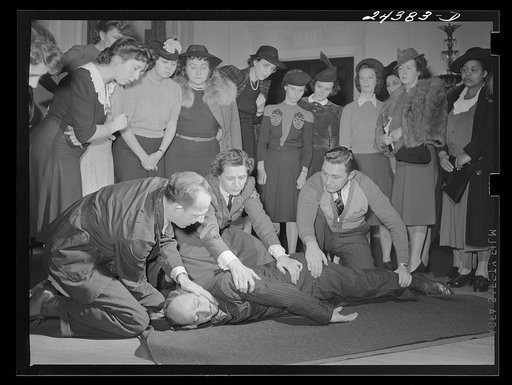 Civilian defense volunteers receiving instruction in proper care for man with spine injury. The first aid class of the American Red Cross, at New York City