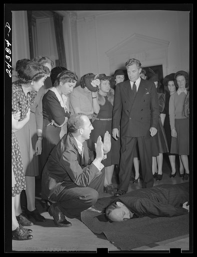 Civilian defense volunteers receiving instruction in proper care for man with spine injury. First aid class. American Red Cross, New York City