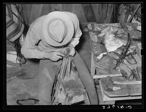 Cowhand working with leather in saddle room. Quarter Circle 'U' Ranch, Montana