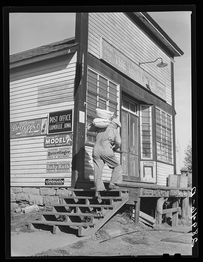 Untitled photo, possibly related to: Carrying bags of flour out of general store. Lamoille, Iowa
