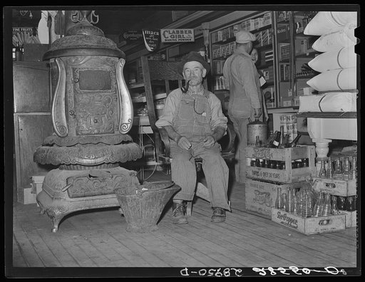 Farmer sits near the stove. General store. Lamoille, Iowa