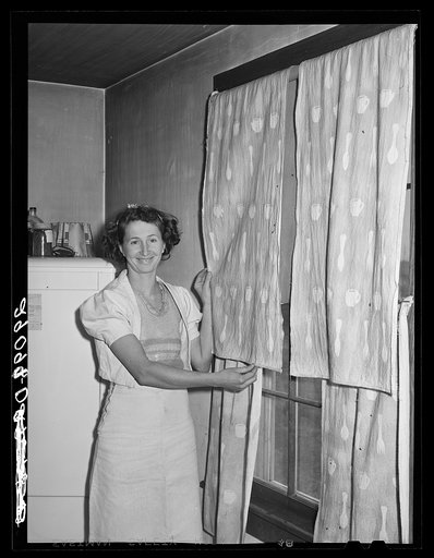 The FSA (Farm Security Administration) home supervisor has helped this woman make her dress of flour sacks and decorate her curtain with splatter work. Osage Farms, Missouri