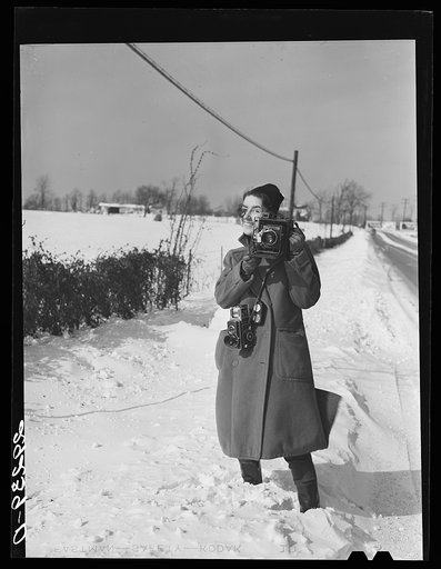 Untitled negative showing Marion Post Wolcott smiling while she stands in snow with two cameras at a farm in Montgomery County, Maryland