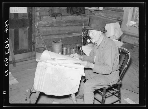 William Besson, iron ore prospector, examining geological survey maps in his cabin near Winton, Minnesota