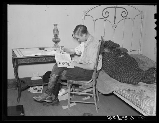 Boy reading in bedroom. Note lack of proper bed clothing. Home of A.O. Ryland near Williston, North Dakota
