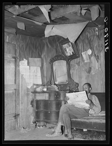 Sharecropper reading newspaper in corner of living room. Note the bureau and ceiling. Near Southeast Missouri Farms