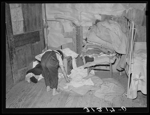 Southeast Missouri Farms. Child picking up clothes in corner of bedroom of shack home. Note lack of storage facilities