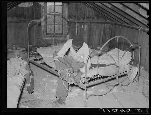 New Madrid County, Missouri. Son of sharecropper putting on shoes in attic bedroom of his home