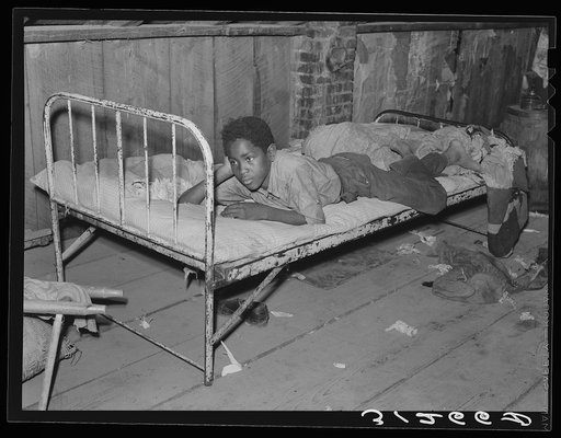Boy resting on bed in attic of sharecropper shack. New Madrid County, Missouri