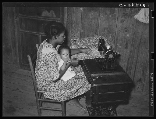 Wife of sharecropper, with baby in her lap, at sewing machine. Family will work under tenant purchase program. Near Caruthersville, Missouri