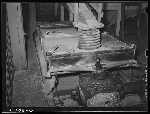 Worker cleaning disks of machine used to separate husks from kernel in rice mill operation. State rice mill, Crowley, Louisiana