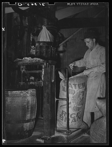 Sewing bag of rice brand after being weighed in rice packaging process. Crowley, Louisiana