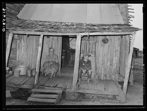 Aged couple sitting on front porch of farm home near Crowley, Louisiana