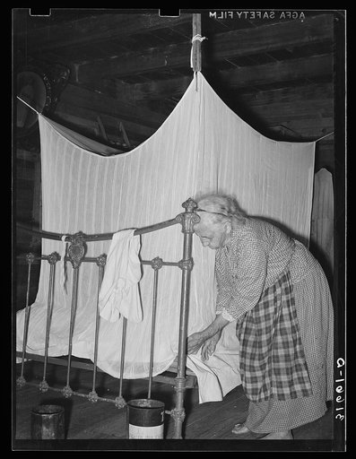 Aged Cajun woman tucking in mosquito bar under mattress. Near Crowley, Louisiana