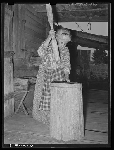 Aged Cajun woman using crude mortar and pestle in process of hulling rice. Near Crowley, Louisiana