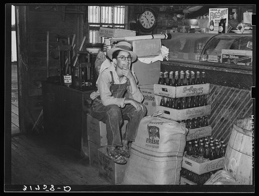 Farm boy sitting on cartons in general store. Jarreau, Louisiana
