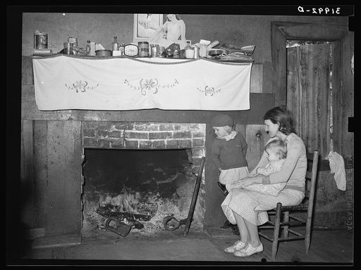 Mrs. Bagget and two children in front of fireplace. Note the board window. Laurel, Mississippi