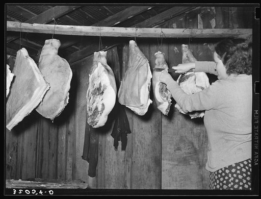 Wife of tenant farmer cutting piece of ham in smokehouse near Pace, Mississippi. Background photo for Sunflower Plantation