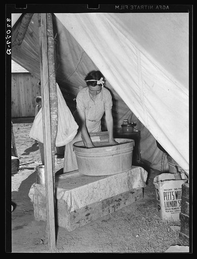 Migrant white mother washing clothes in front of tent home. Weslaco, Texas. See general caption