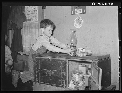 Son of migrant worker reaching for lamp atop cabinet in trailer home. Weslaco, Texas. See caption 32108-D
