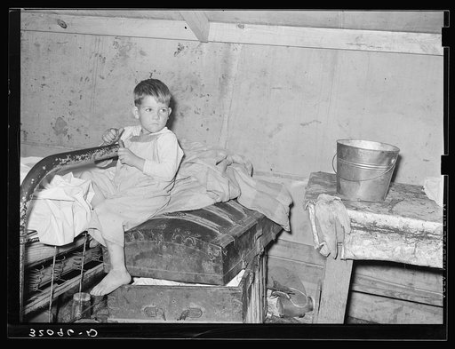 Son of white migrants sitting on trunk in tent home. Weslaco, Texas. See caption 32108-D