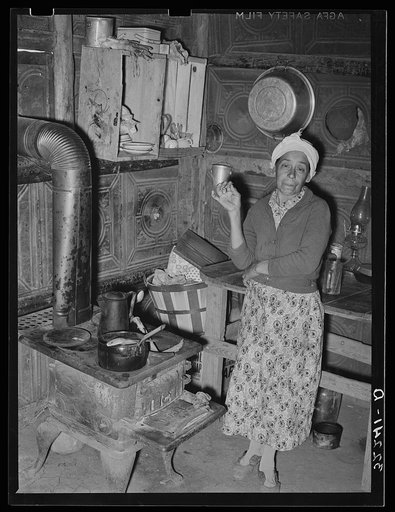 Untitled photo, possibly related to: Mexican woman in kitchen corner of her one-room dwelling made out of discarded tin ceiling material. Notice dirt floor. Robstown, Texas