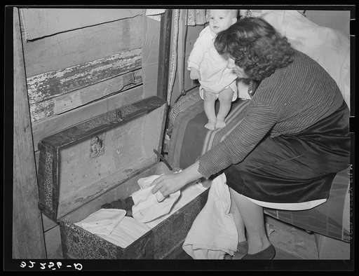 White migrant woman taking out garments for baby. Shantytown on Nueces Bay, Corpus Christi, Texas