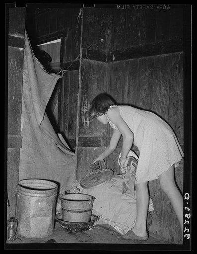 Mexican girl standing over pan of hot coal in which pail of water is heating. Robstown, Texas