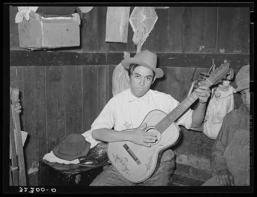 Mexican boy playing guitar in room of corral. Robstown, Texas
