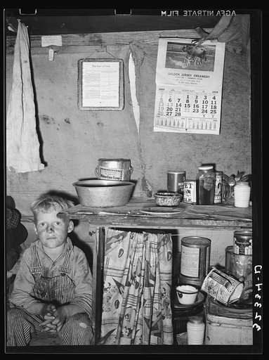 Child of migrant sitting by kitchen cabinet in tent home near Edinburg, Texas