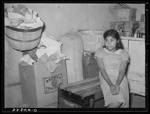Mexican girl sitting in corner of combined living room and kitchen. Crystal City, Texas