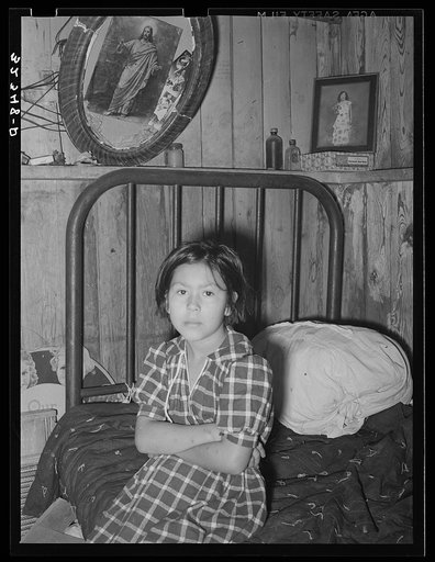Mexican girl sitting on bed. Crystal City, Texas