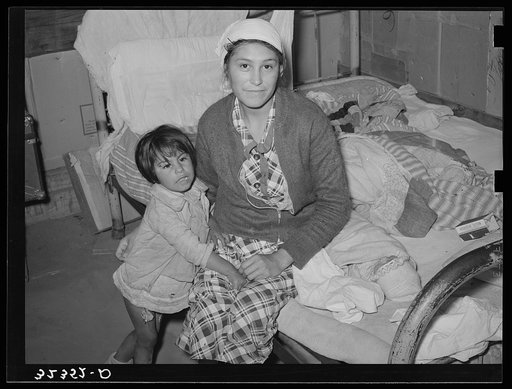 Mexican mother and child in home. Crystal City, Texas. This woman had given birth to baby on bed while she had an advanced case of gonorrhea. The baby at time picture was taken was ten days old. The baby slept in the same bed with the mother and she was caring for both it and the small child by her 