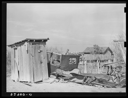 Privy and wrecked automobile in backyard of Mexican home. Old automobile parts are saved for use in construction of fences, sheds and houses. Crystal City, Texas