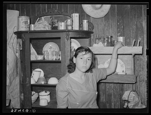 Mexican girl standing in front of dish cupboard. San Antonio, Texas