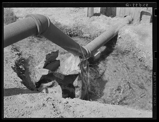 Water running from pipe into irrigation ditch. La Pryor, Texas