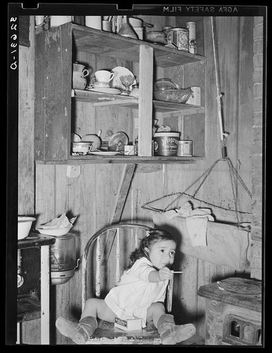 Mexican child in kitchen. San Antonio, Texas. Notice the basket swing suspended from the ceiling