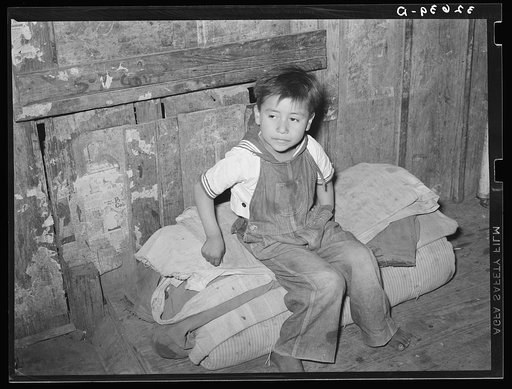 Mexican boy sitting on bedroll. These rolls are used on the floor for beds at night, rolled up during the day. San Antonio, Texas
