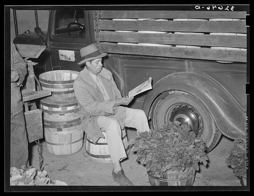 Mexican spinach peddler reading the newspaper about 4:30 in the morning. San Antonio, Texas