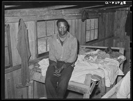 Negro strawberry worker sitting on end of bunk in bunkhouse. Hammond, Louisiana