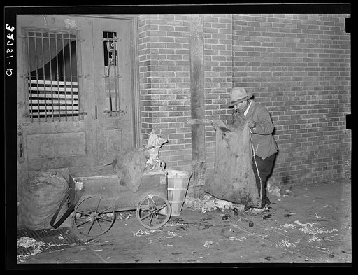 Mexican man gathering refuse at early morning vegetables market. San Antonio, Texas. He will use this to feed hogs