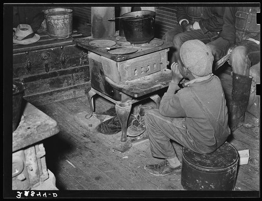 Negro boy sitting by the stove on a cold day in the strawberry picking season. Near Independence, Louisiana